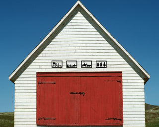 A white barn with a red door and cowboy themed metal art above the doors.