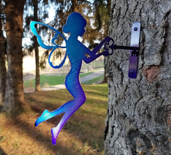 A blue metal fairy holding a key and screwed into a tree.