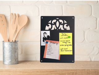 A kitchen counter with black memo board with a scroll design cut out. It has lists and photos attached to it with magnets.