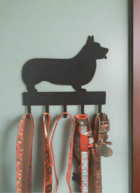 Dog silhouette wall hook with multiple dog collars and leashes attached on a light beige wall.
