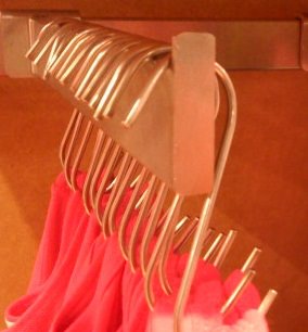 A row of metal S-shaped hooks on a rail with clothes on the hooks