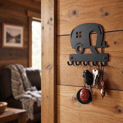 A metal camper-shaped key holder mounted on a rustic wooden wall, holding several keys in a cozy interior setting.