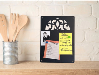 A kitchen counter with black memo board with a scroll design cut out. It has lists and photos attached to it with magnets.