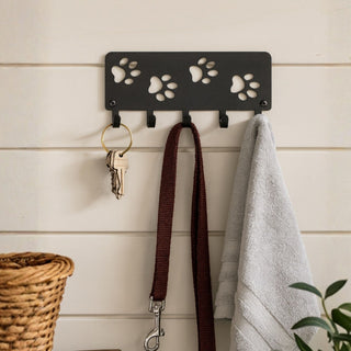 Wall-mounted hook with paw print design holding a key, leash, and towel against a wooden panel background.
