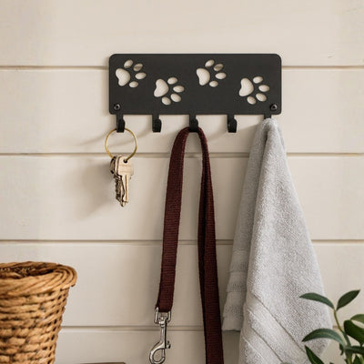 Wall-mounted hook with paw print design holding a key, leash, and towel against a wooden panel background.