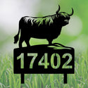 A black metal yard sign featuring a Highland cow silhouette on top of a rectangular base with the number 17402, shown against a blurred green grass background.