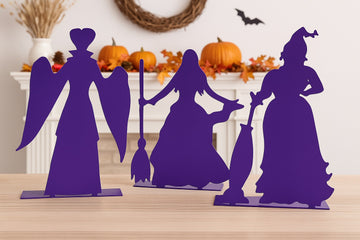 Silhouettes of 3 purple witches on a table with Halloween decorations in the background.