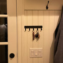 A plain metal flat bar with 5 hooks for hanging keys.