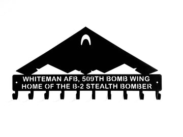 A black metal key holder shaped like a B-2 Stealth Bomber with the text 'WHITEMAN AFB, 509TH BOMB WING HOME OF THE B-2 STEALTH BOMBER' on a white background