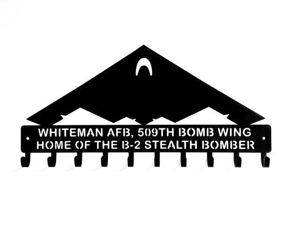 A black metal key holder shaped like a B-2 Stealth Bomber with the text 'WHITEMAN AFB, 509TH BOMB WING HOME OF THE B-2 STEALTH BOMBER' on a white background
