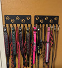 Two black metal dog collar and leash racks mounted on a textured orange wall, holding multiple colorful dog leashes and collars.