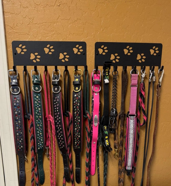 Two black metal dog collar and leash racks mounted on a textured orange wall, holding multiple colorful dog leashes and collars.