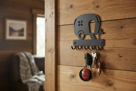 A metal camper-shaped key holder mounted on a rustic wooden wall, holding several keys in a cozy interior setting.