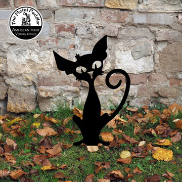 Black metal cat sculpture on grass with stone wall background