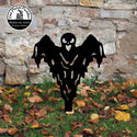 Black ghost-shaped decorative yard art in front of a stone wall with fallen leaves on the ground.