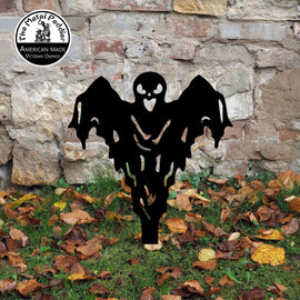 Black ghost-shaped decorative yard art in front of a stone wall with fallen leaves on the ground.