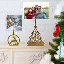 Decorative Christmas tree and reindeer ornament on a mantelpiece with family photo and snowy village scene in the background.