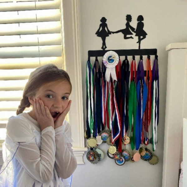 Irish dancer key hanger filled with medals and a young girl looks excited.
