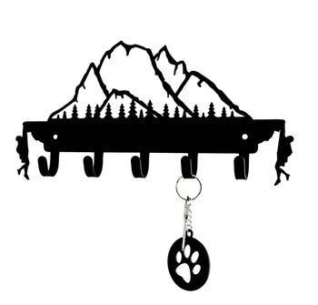 Metal key holder featuring a mountain and forest design, with a key and paw print keychain hanging from one of the hooks