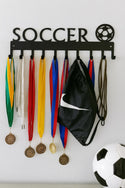 Soccer-themed medal holder with medals, a black bag, and a soccer ball on a white wall.