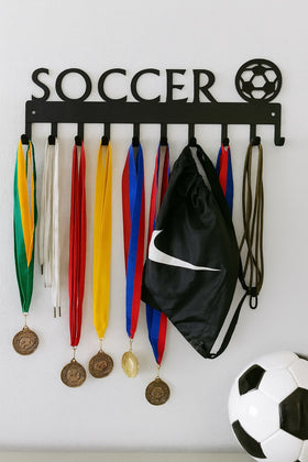 Soccer-themed medal holder with medals, a black bag, and a soccer ball on a white wall.