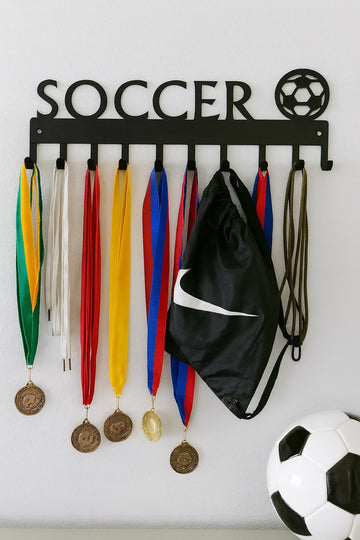 Soccer-themed medal holder with medals, a black bag, and a soccer ball on a white wall.