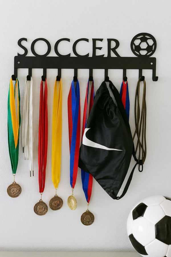 Soccer-themed medal holder with medals, a black bag, and a soccer ball on a white wall.
