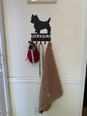A leash holder with the silhouette of a Yorkshire terrier dog, Maximus, and his harness, leash and towel on the hooks.
