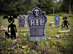 Halloween-themed graveyard scene with tombstones and metal zombie figures in a grassy field.