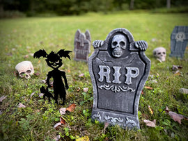 Halloween-themed decorations including a skeleton figure, black silhouette of a child with bat wings, and a gravestone with 'RIP' on a grassy field.